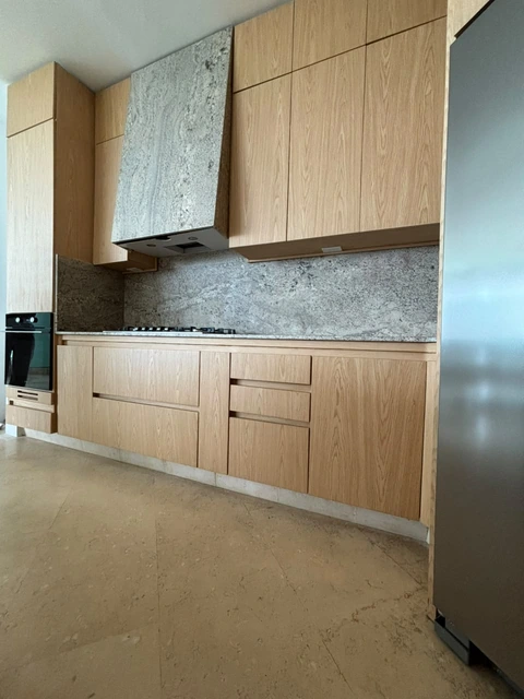Frente de cocción de la cocina entregada por PyP, con mobiliario en tonos madera claros y frentes sin manijas