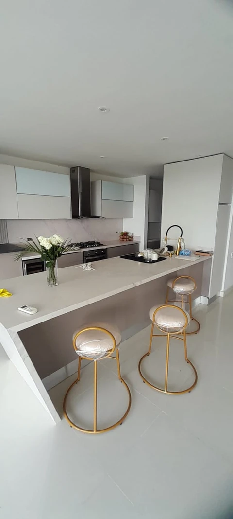 Cocina real de PyP con península clara, muebles altos y tres sillas de estructura dorada